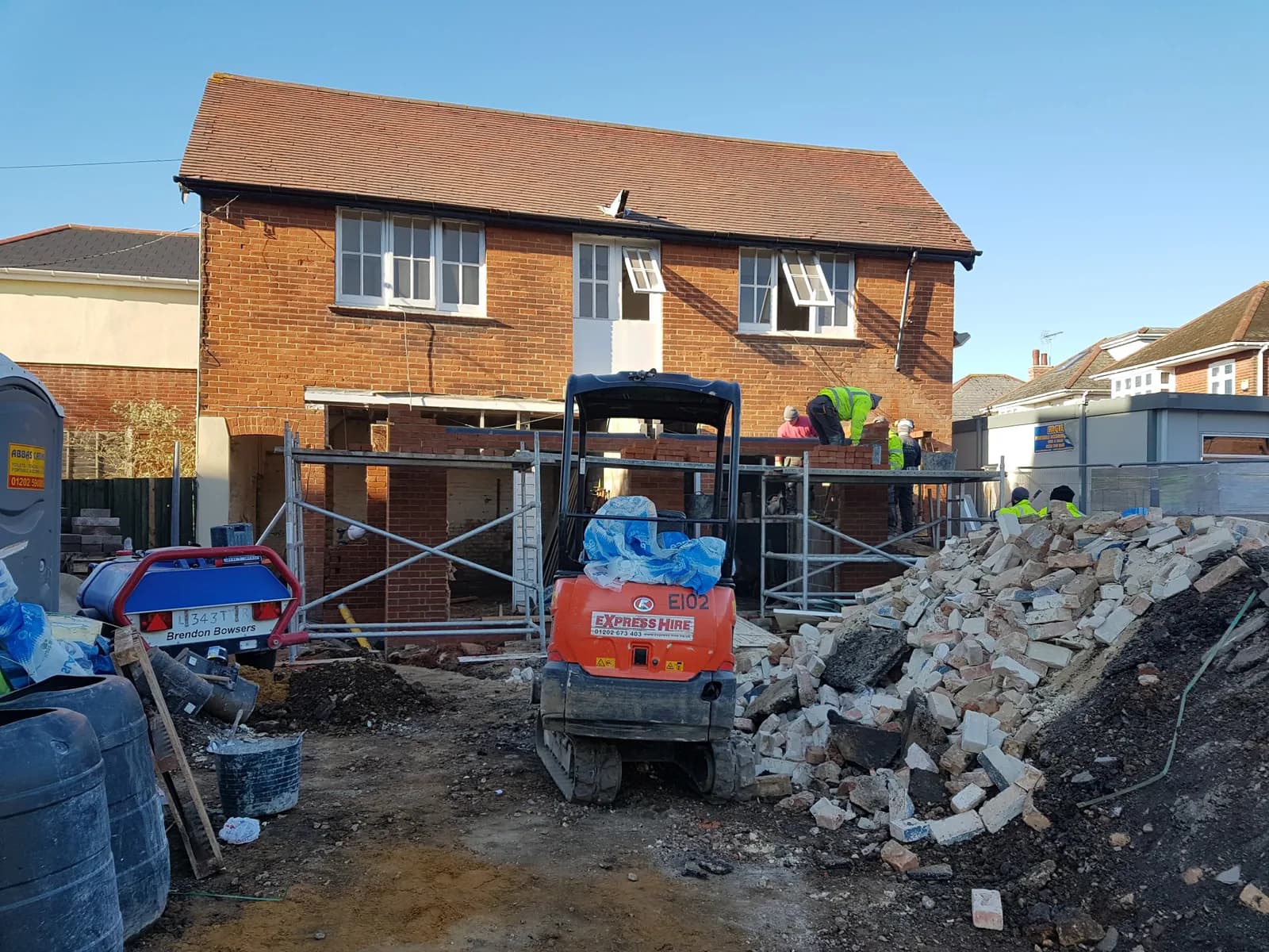 Brick residential build with scaffold, workers, rubble and mini digger