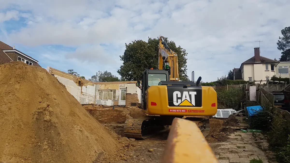 CAT excavator beside mound of excavated soil and partially demolished house