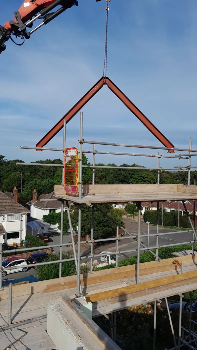 Crane lifting a triangular red steel frame above scaffold on a residential site