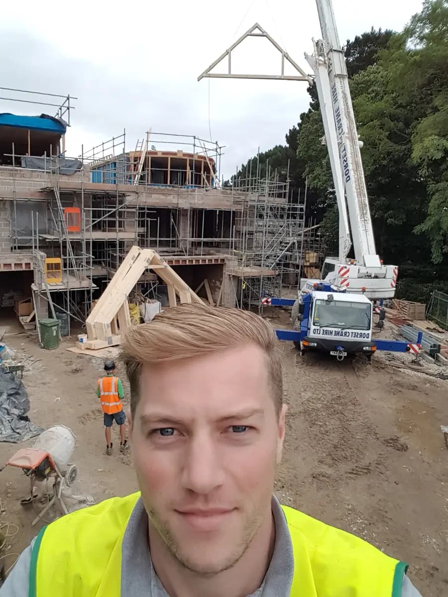 Crane lifting timber roof truss onto scaffolded building frame