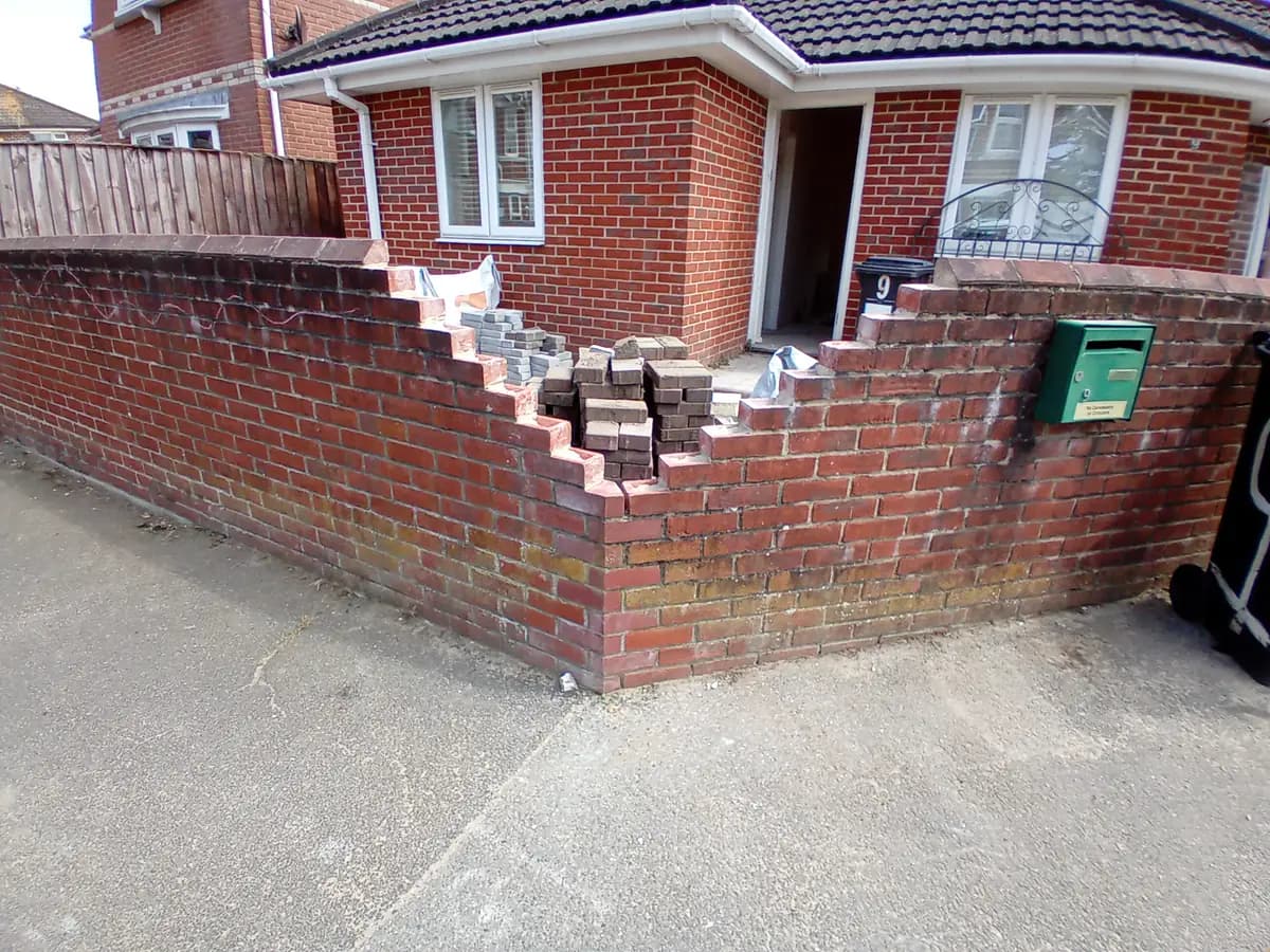 Part-built brick boundary wall with stacks of bricks outside a house