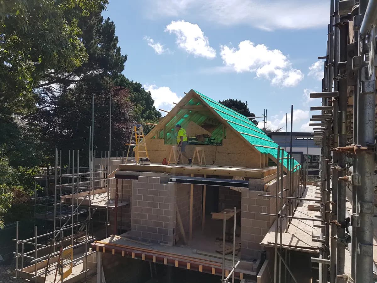 Timber roof rafters with green membrane, scaffolding and workers