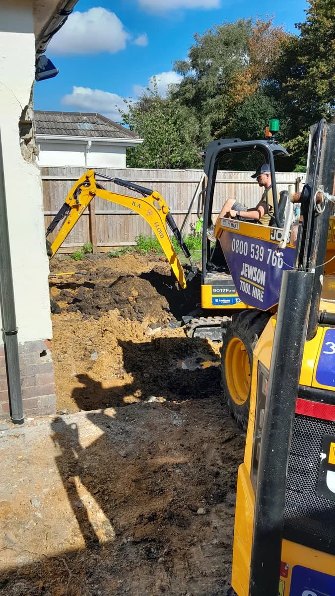 Mini excavator digging beside a house wall during groundwork