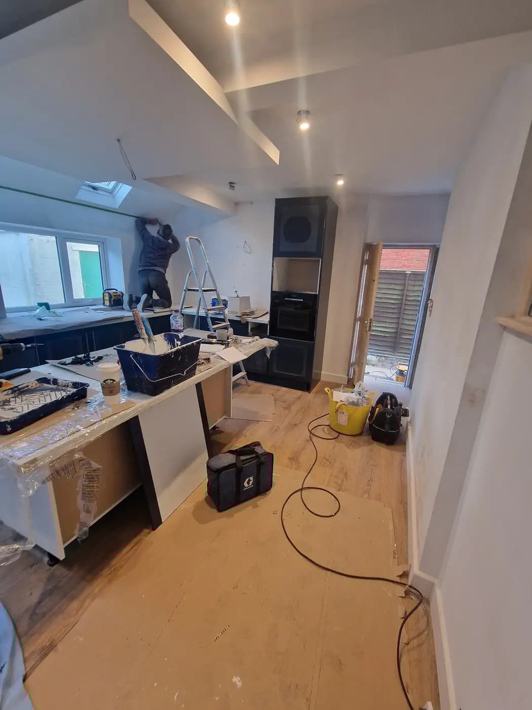 Kitchen renovation with fitted dark base units, lit ceiling and worker near window