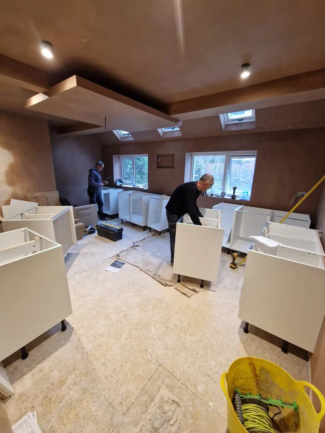 Kitchen installation with white cabinet carcasses, workers and tools