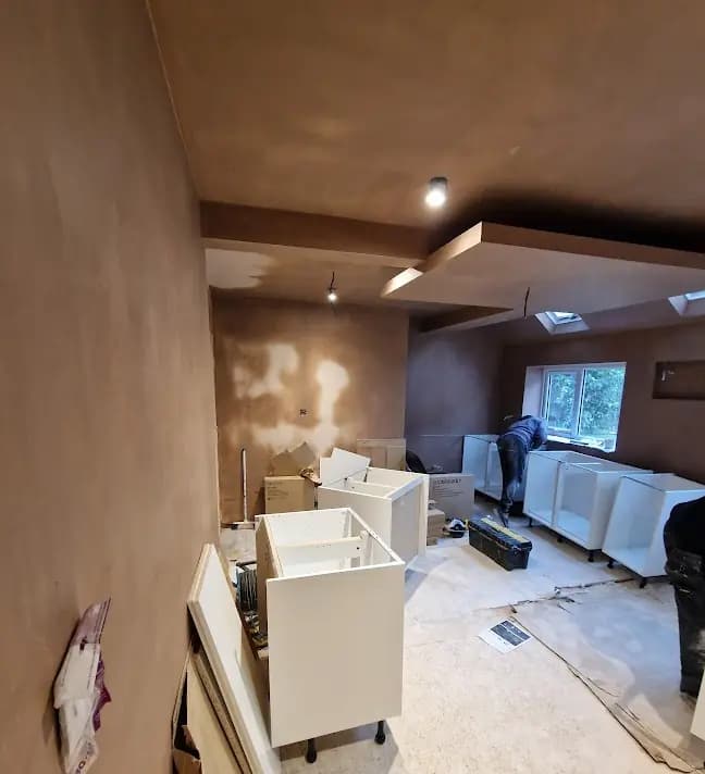 Kitchen installation with brown plaster walls, cabinet units and worker at far window