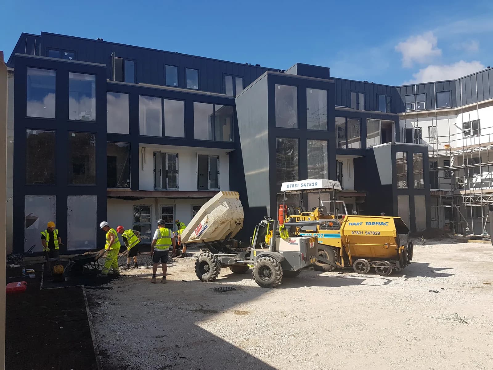 Modern dark-clad building with workers and tarmac works outside
