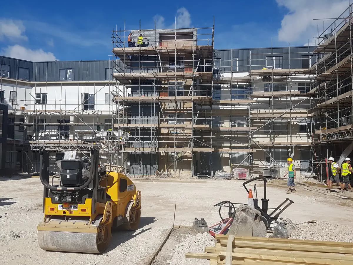 Road roller and workers beside a scaffolded multi-storey construction project