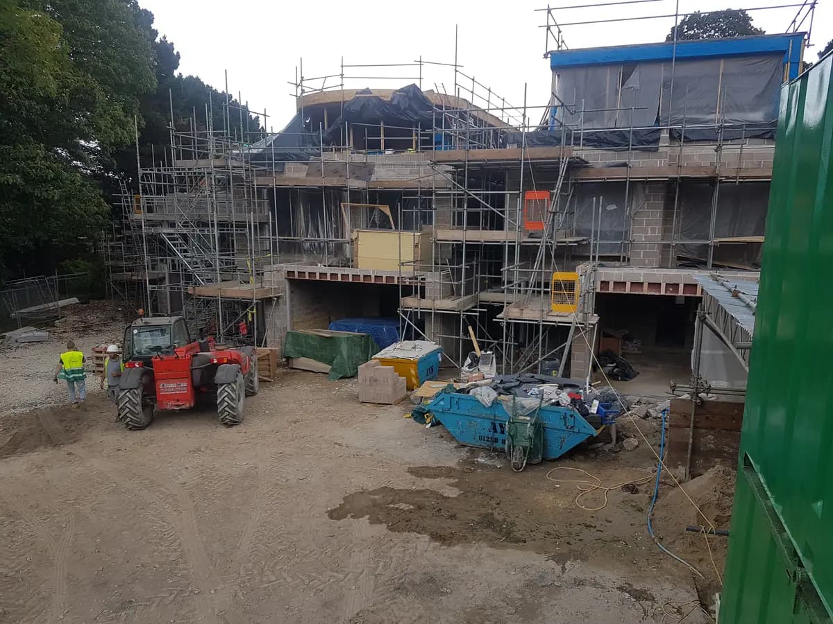 Red telehandler on muddy construction site with scaffolding and blockwork