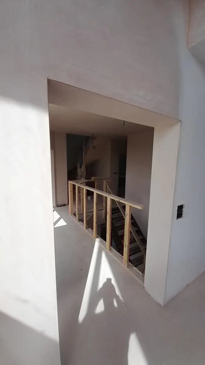 Unfinished stairwell with plastered walls and temporary wooden safety railing