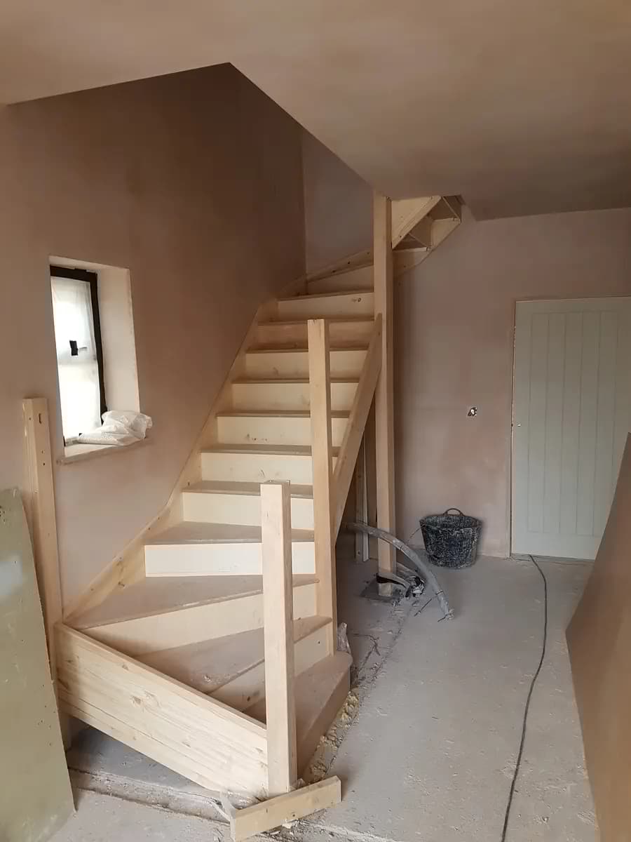 Interior timber staircase under construction with new plastered walls