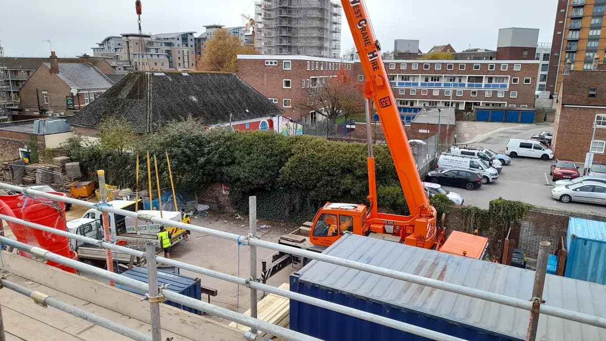 Orange crane lifting materials on urban construction site viewed from scaffold