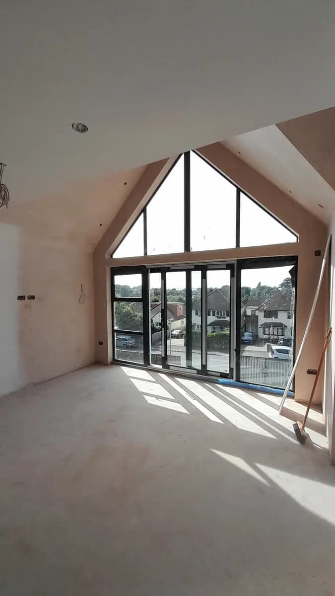 Unfinished vaulted room with large dark-framed gable glazing and plastered walls