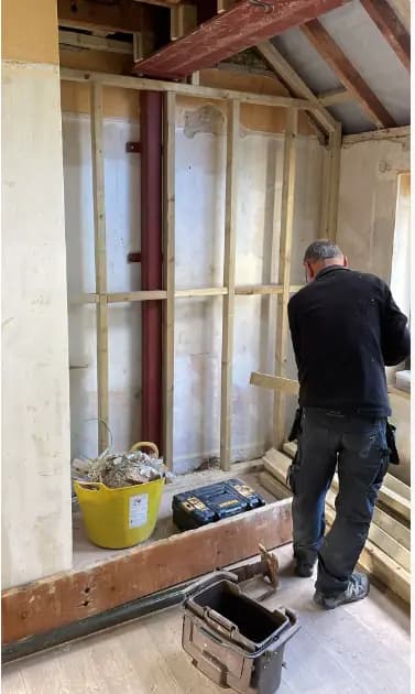 Worker inside an attic renovation with exposed framing, tools and debris